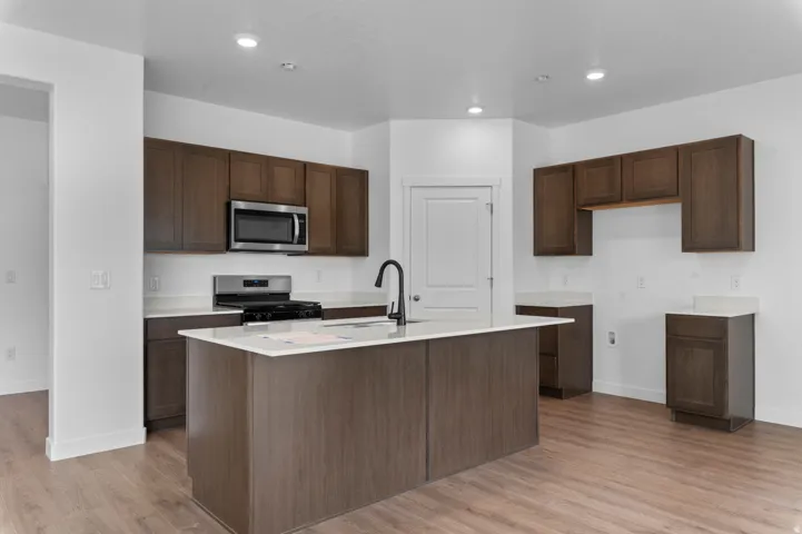 Modern kitchen featuring a central island with a matte black faucet, dark wood-finish cabinetry, and stainless steel appliances including a microwave and gas range