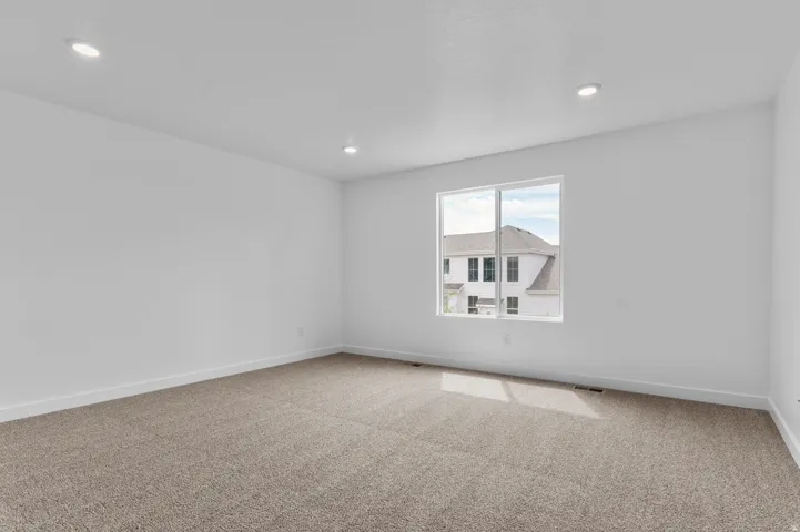 Spacious room featuring neutral carpet flooring, recessed ceiling lighting, a large window, and white baseboards