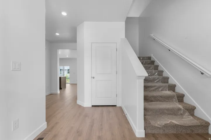 Foyer featuring wood-finish flooring extending into the hallway, a carpeted staircase with white balustrade, white interior doors, and recessed ceiling lighting