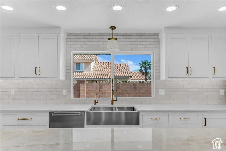 Contemporary kitchen featuring white shaker cabinetry, an apron-front stainless steel sink, a stainless steel dishwasher, light subway tile backsplash, and a gold-tone faucet