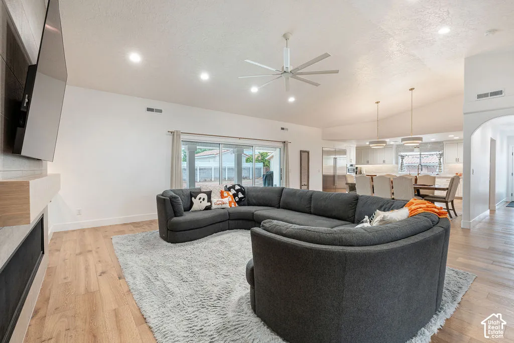 Open-concept living space featuring vaulted ceilings, recessed lighting, wood-finish flooring, a contemporary ceiling fan, and a built-in fireplace with a mantel