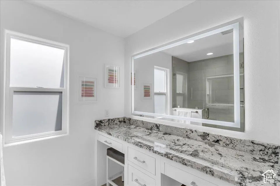 Vanity area featuring a large illuminated mirror, expansive stone countertop, white cabinetry with silver hardware, and a built-in makeup vanity