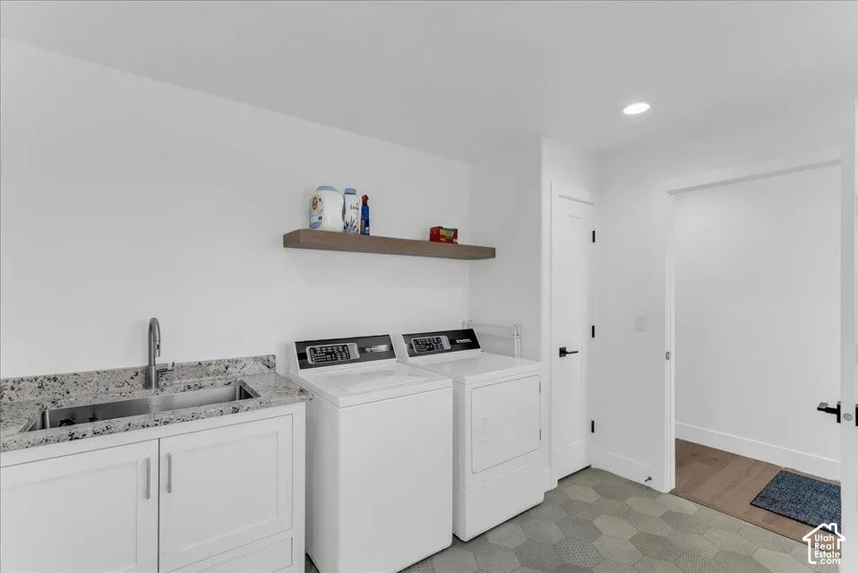Laundry room featuring a stainless steel sink, granite-style countertop, white cabinetry, and a floating wood-finish shelf