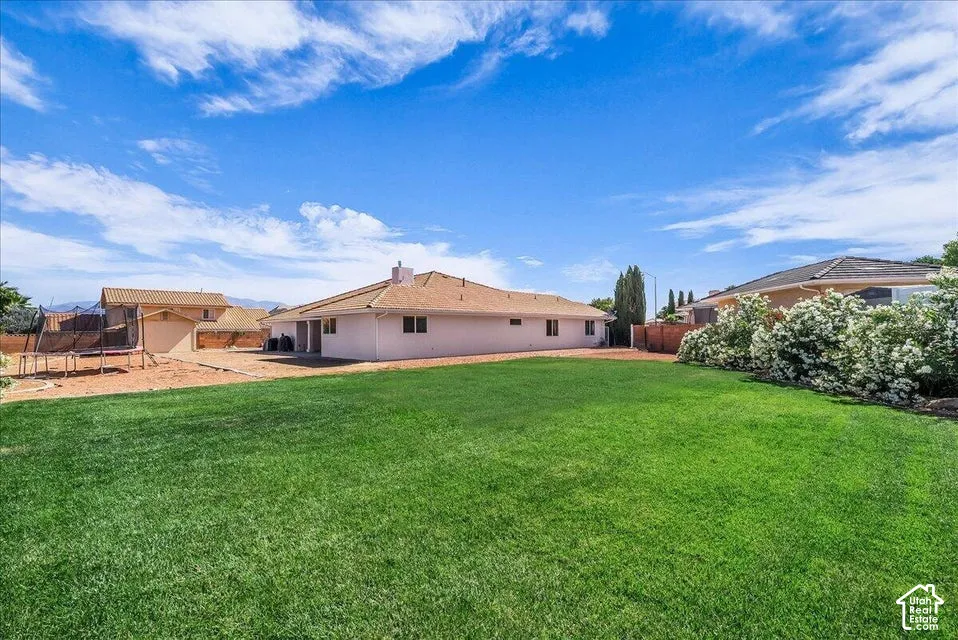 Expansive green lawn with a stucco exterior home featuring a brown shingle roof, multiple windows, and a mature flowering bush