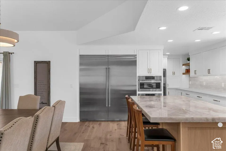 Gourmet kitchen featuring a large stone-top island, integrated stainless steel appliances, white cabinetry with contemporary hardware, and wood-finish flooring