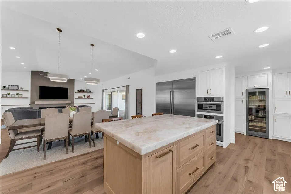 Spacious kitchen and dining area featuring a large center island with a stone countertop, white cabinetry, integrated stainless steel appliances, and wood-finish flooring