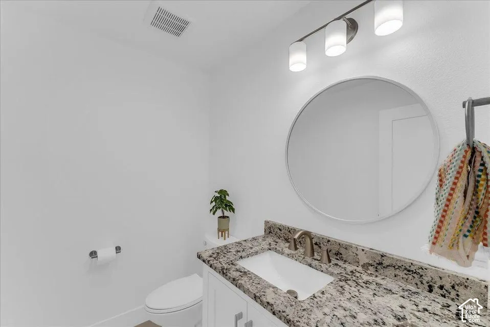 Bathroom featuring a modern circular mirror, three-light vanity fixture, granite countertop, undermount sink, and a white vanity cabinet