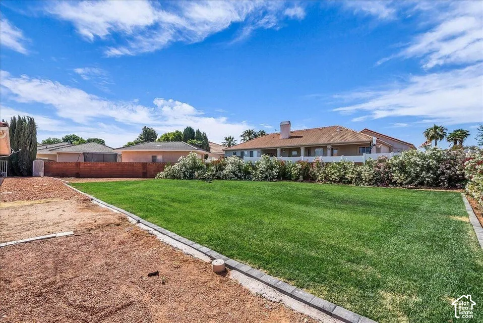 Expansive backyard featuring a lush green lawn, decorative shrubs, and a partial brick retaining wall