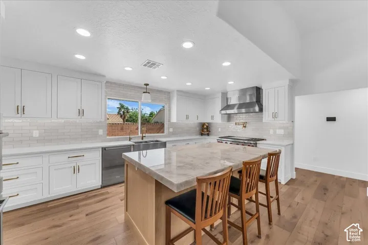 Contemporary kitchen featuring white cabinetry, a large center island with seating, stainless steel appliances including a professional range and hood, and wood-finish flooring