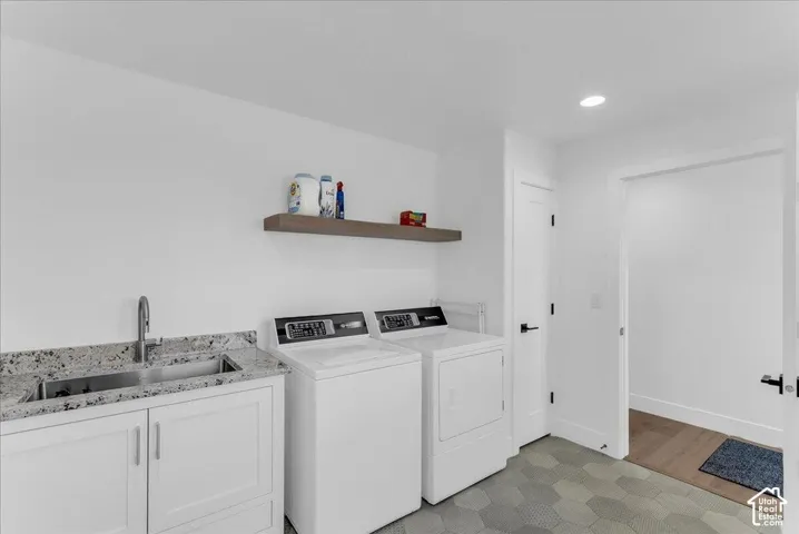 Laundry room featuring a stainless steel sink, granite-style countertop, white cabinetry, and a floating wood-finish shelf