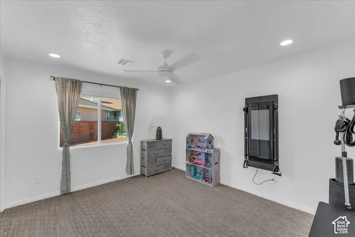Bright room featuring a large window, textured gray carpeting, recessed lighting, and a ceiling fan