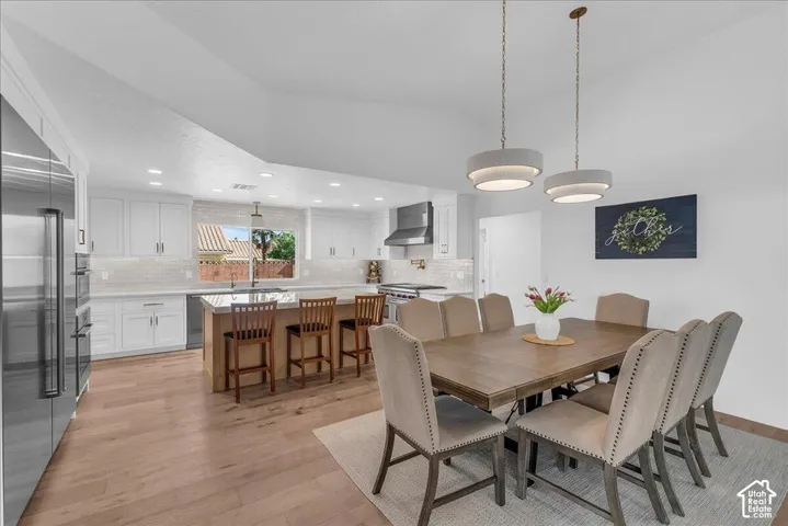 Spacious kitchen and dining area featuring light wood-finish flooring, white cabinetry, a large kitchen island with seating, a stainless steel refrigerator, and dual pendant lighting fixtures