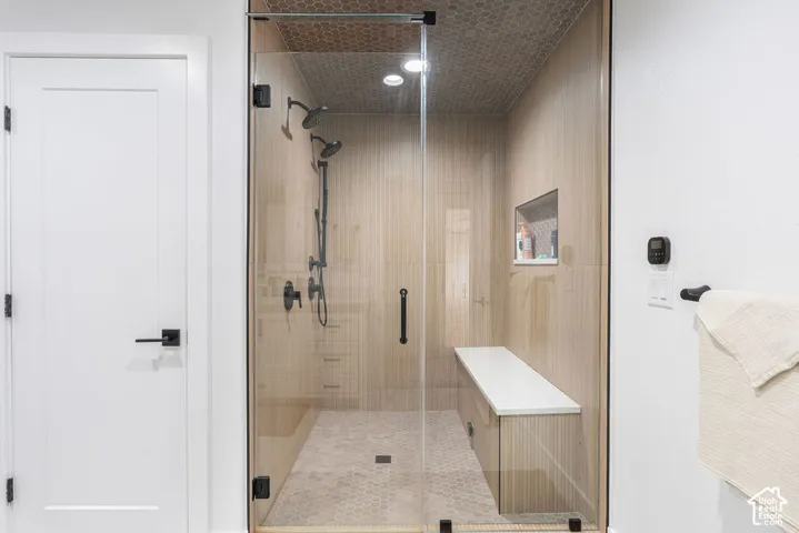 Glass-enclosed shower with multiple showerheads, a built-in bench, and a tiled niche