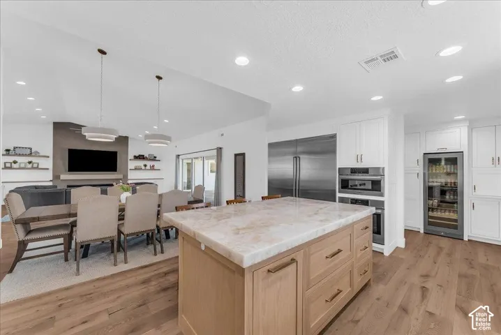 Spacious kitchen and dining area featuring a large center island with a stone countertop, white cabinetry, integrated stainless steel appliances, and wood-finish flooring