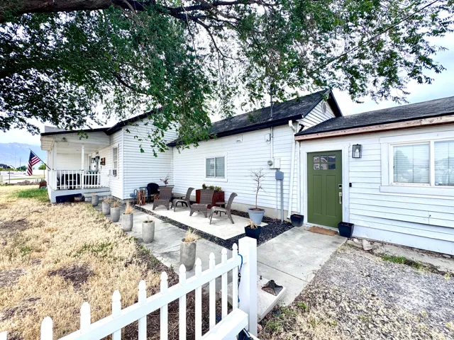 Exterior featuring white siding, a covered porch with white railings, a concrete patio area, a dark olive green entry door with windowpanes, and a white picket fence