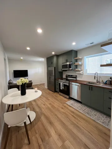 Open-concept kitchen featuring wood-finish flooring, dark green cabinetry with black hardware, stainless steel appliances, and a wood-finish countertop