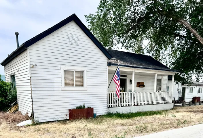 Single-story residence featuring white horizontal siding, a covered front porch with white railing, and a black shingle roof