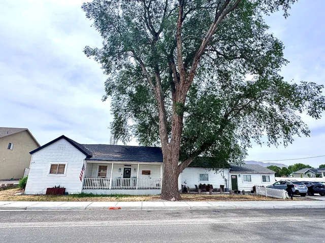 White siding residence featuring a covered front porch with white railings, a prominent mature tree, and a dark shingled roof