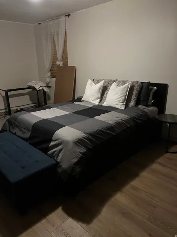 Room featuring wood-finish flooring, neutral wall paint, and a window with blinds and sheer drapes