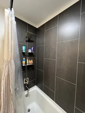 Bathtub with dark rectangular wall tiling, brushed chrome fixtures, and a ceiling-mounted rain shower head