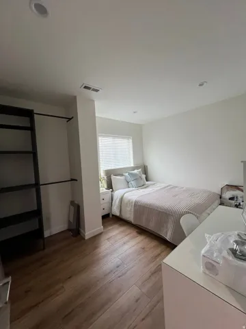Bedroom featuring wood-finish flooring, recessed lighting, a window with blinds, and an open closet system with shelving and a hanging rod