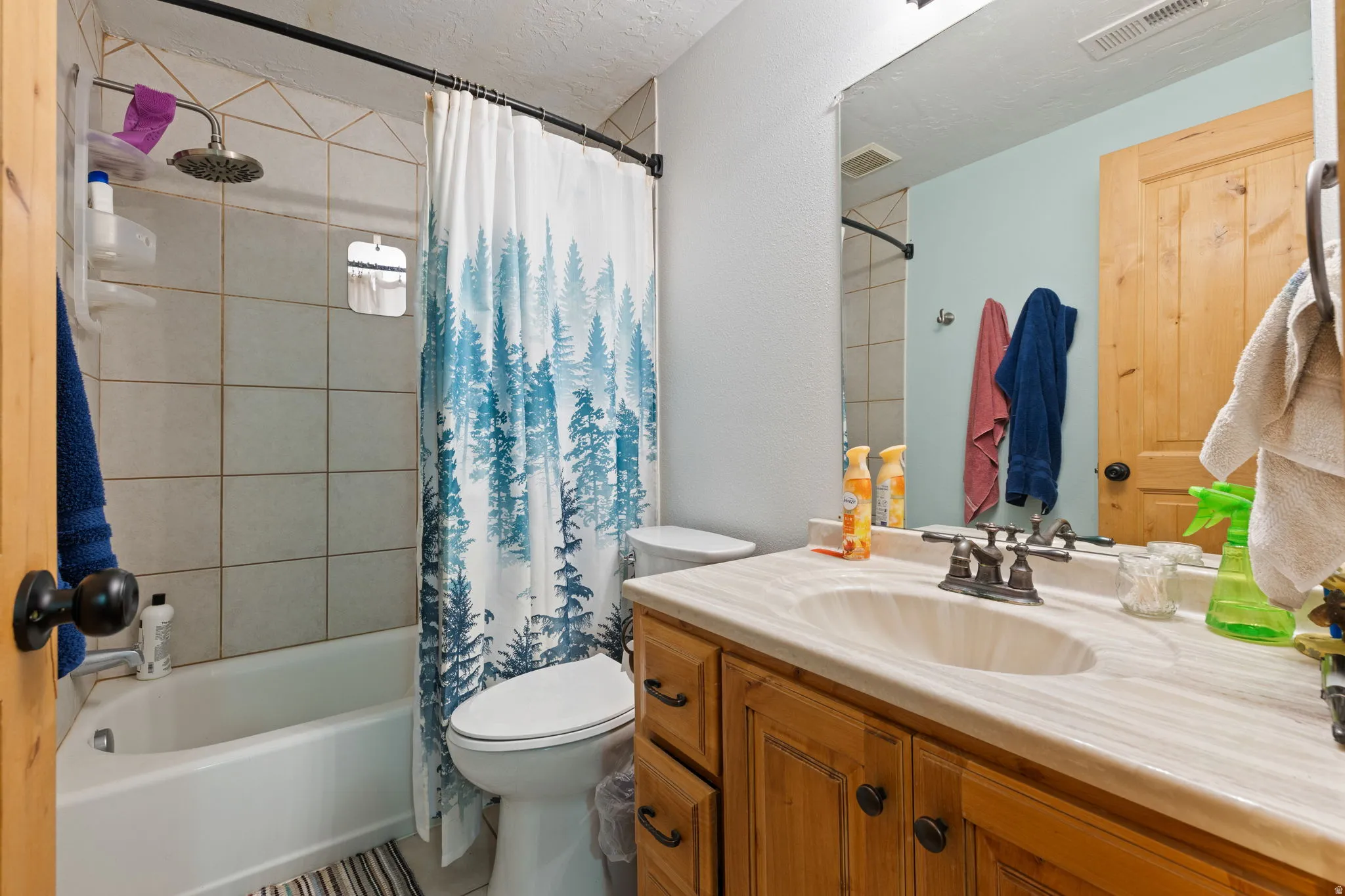 Bathroom featuring a wood vanity with an integrated sink, a large wall-mounted mirror, a toilet, and a shower-over-tub with tile surround