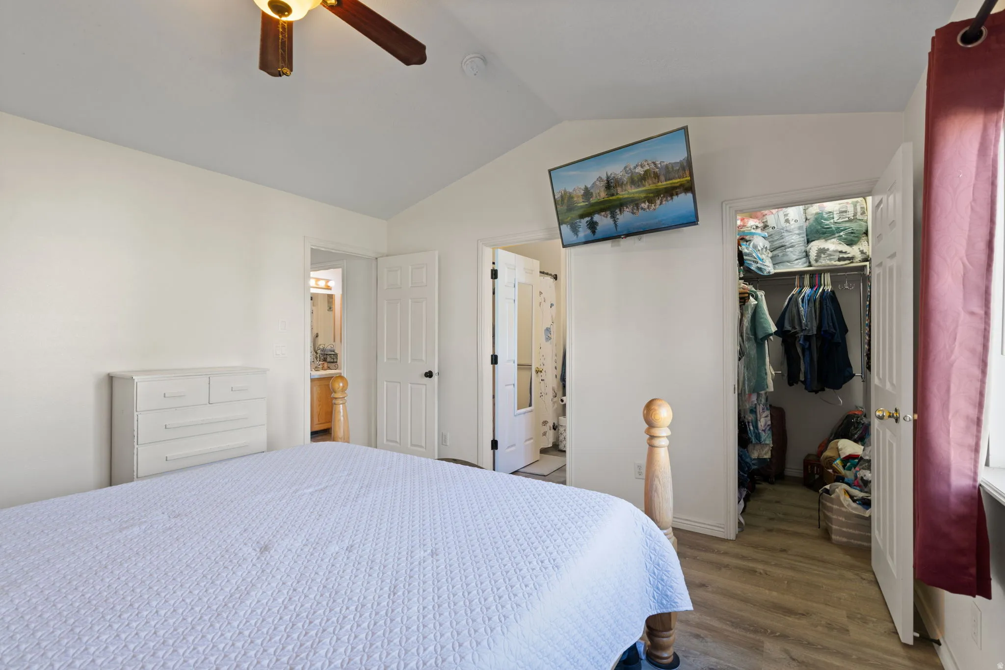 Vaulted ceiling bedroom with wood-finish flooring, an open closet, and a ceiling fan
