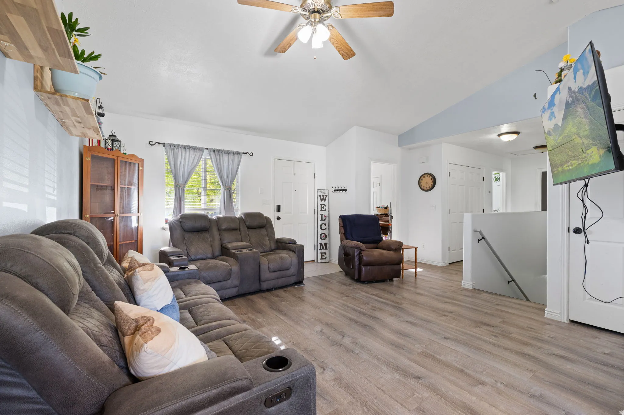 Spacious living area featuring wood-finish flooring, vaulted ceilings, and a ceiling fan with light fixture