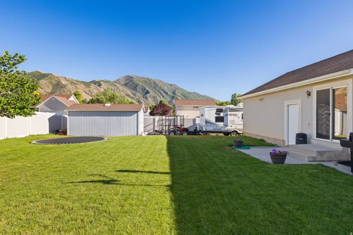 Expansive backyard featuring a manicured lawn, white privacy fencing, and mountain scenery