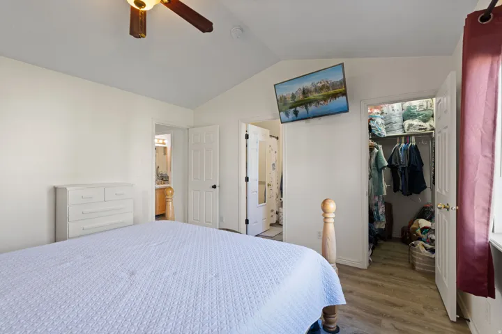 Vaulted ceiling bedroom with wood-finish flooring, an open closet, and a ceiling fan