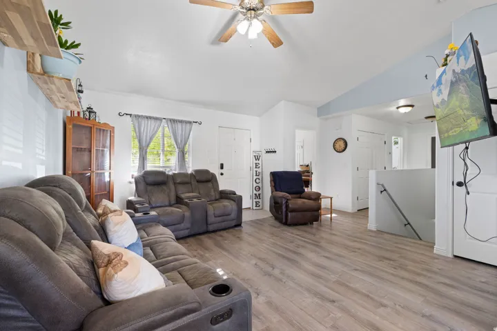 Spacious living area featuring wood-finish flooring, vaulted ceilings, and a ceiling fan with light fixture
