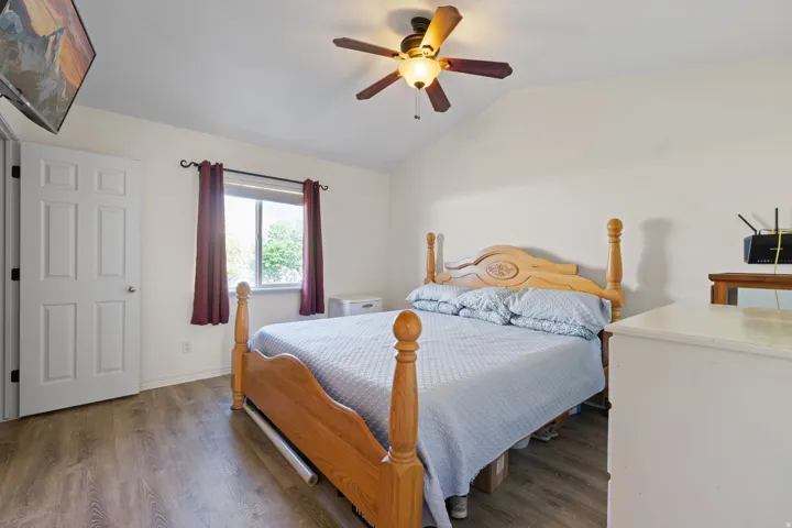 Room featuring vaulted ceilings, wood-finish flooring, a ceiling fan with integrated lighting, and a paneled white door