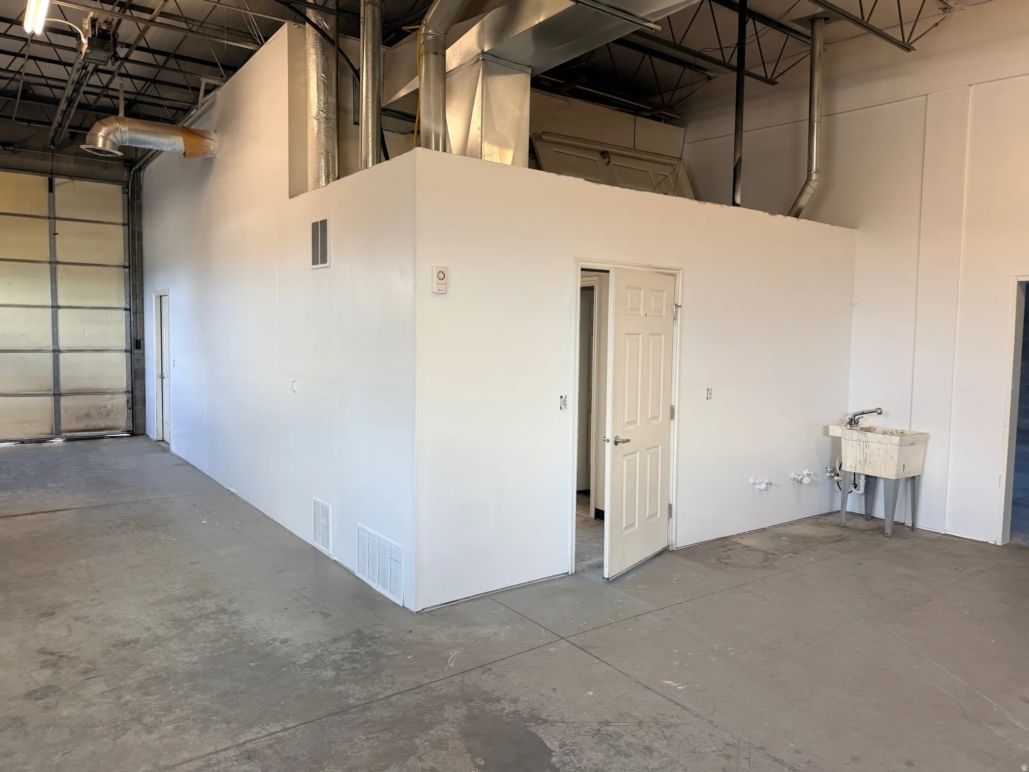 Spacious industrial interior featuring a large roll-up door, exposed ceiling trusses, and visible ductwork