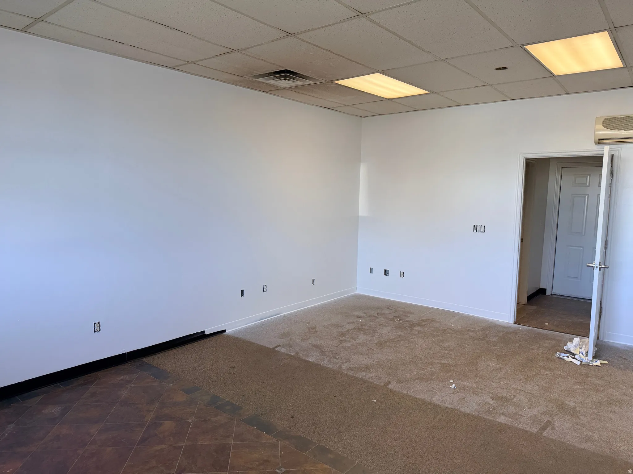 Spacious room featuring white painted walls, a drop ceiling with integrated lighting, and a partially tiled, partially carpeted floor
