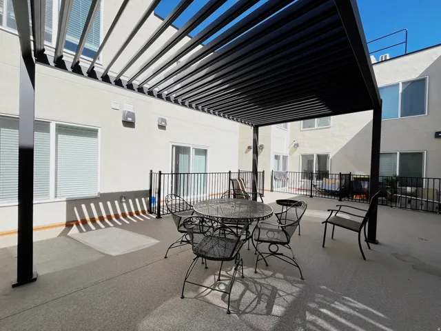 Spacious outdoor patio featuring a modern black metal pergola with adjustable louvered roof, durable concrete flooring, and black metal perimeter railing