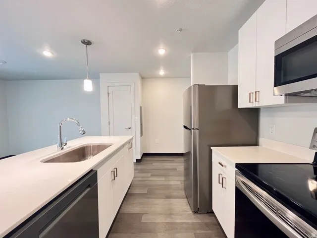 Kitchen featuring white cabinetry, stainless steel appliances, a large island with an undermount sink, and wood-finish flooring