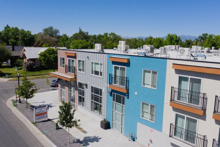 Modern multi-story building featuring varied paneling, vibrant blue and neutral-toned exterior walls, and multiple private balconies with black railings