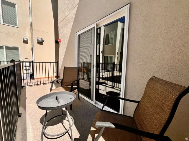 Private balcony featuring a stucco exterior, dark metal railings, and a sliding glass door with a screen