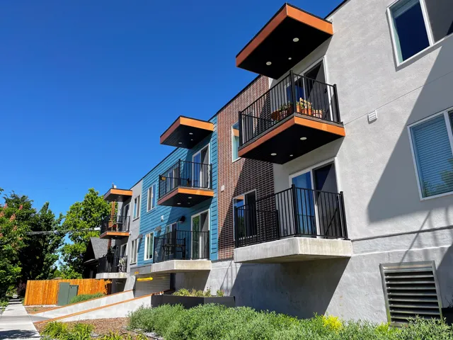 Modern multi-story building featuring balconies with black railings, wood-finish soffits, and recessed lighting
