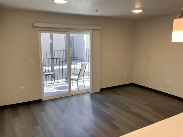 Spacious room featuring wood-finish flooring, light-toned walls, and a sliding glass door providing access to an outdoor balcony with metal railings