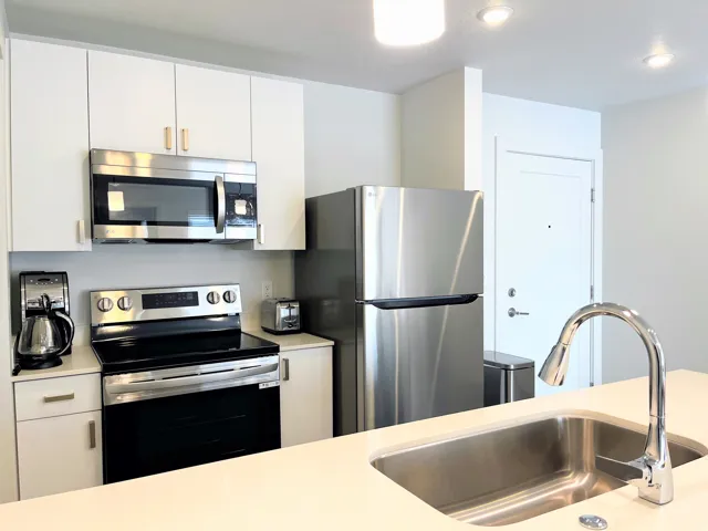 Modern kitchen featuring stainless steel appliances, white cabinetry, a large kitchen sink with a gooseneck faucet, light-toned countertops, and recessed lighting