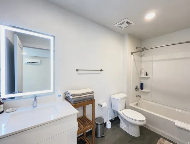 Bathroom featuring a white vanity with an integrated sink, an illuminated mirror, a white toilet, and a white tub with shower