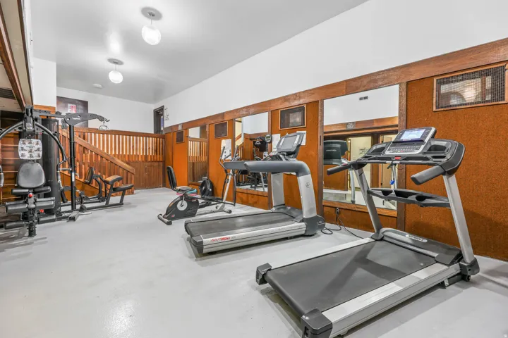 Dedicated fitness space featuring light-toned flooring, recessed lighting, wood-paneled walls, and a built-in mirror