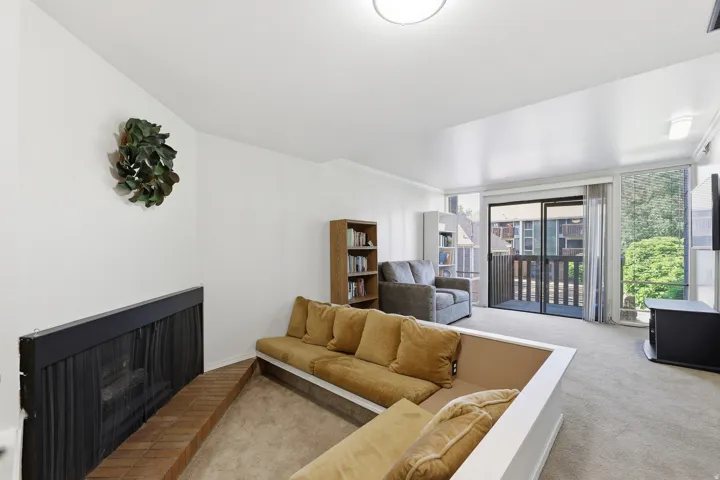 Living area featuring a fireplace with brick hearth, carpeted flooring, and a sliding glass door opening to an outdoor balcony