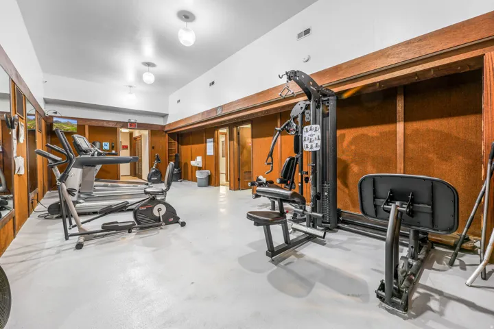 Dedicated fitness room featuring white-painted flooring, wood-paneled walls, and bright overhead lighting