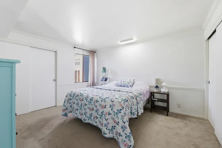 Spacious sleeping area with light-colored carpeting, a window with natural illumination, and a built-in closet featuring sliding doors