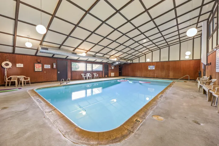 Indoor swimming pool featuring an angled paneled ceiling, wood-paneled walls, and multiple globe light fixtures