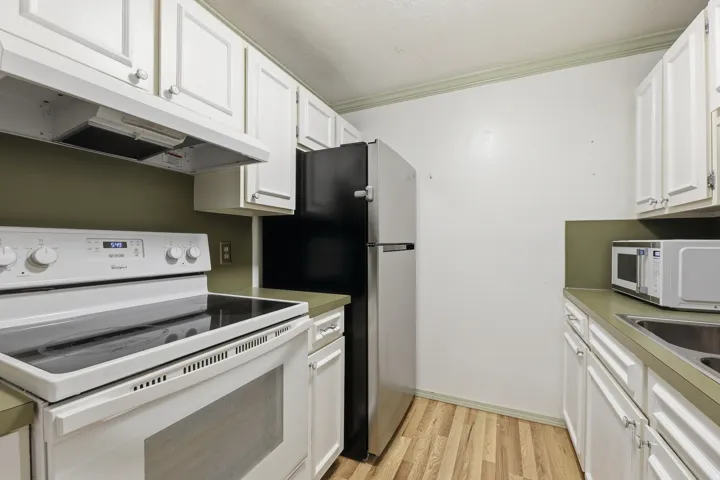 Kitchen featuring white cabinetry, light countertops, wood-finish flooring, and a white electric range with an overhead exhaust fan