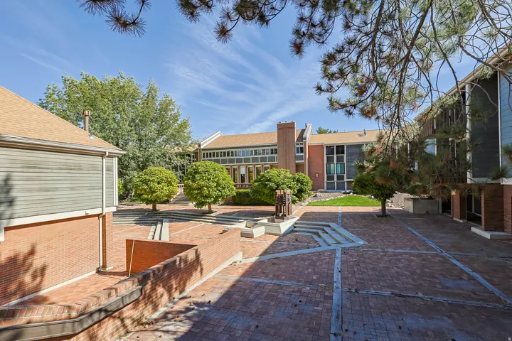 Expansive brick paver courtyard with tiered concrete steps, surrounded by mature trees and multi-level buildings featuring brick and siding exteriors