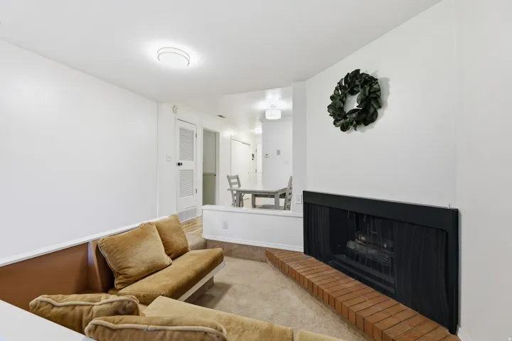 Carpeted living area featuring a brick hearth fireplace, built-in wall seating, and an elevated dining area